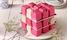 a stack of pink and white cakes sitting on top of a plate next to silver utensils