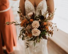 a bride holding a bouquet of flowers in her hand and another woman standing behind her