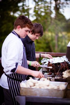 two men preparing food on an outdoor grill