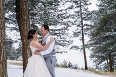 a bride and groom standing next to each other in the snow near some tall trees