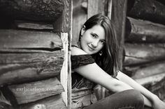 a young woman leaning against a log cabin wall posing for a black and white photo