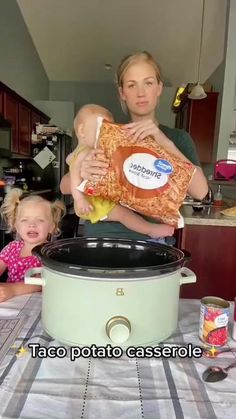 a woman holding a baby while standing next to a crock pot