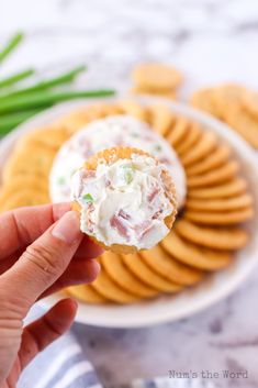 a hand holding a cracker filled with crab salad on top of crackers next to green beans