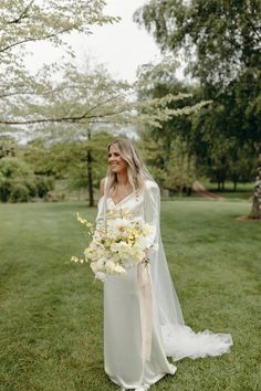 a woman standing in the grass holding a bouquet