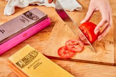 a person cutting tomatoes on top of a wooden cutting board next to a book and knife