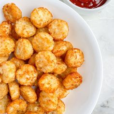 a white plate topped with tater tots next to a bowl of ketchup