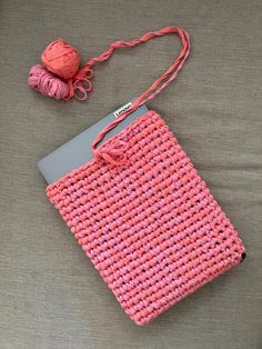 a crocheted pink purse sitting on top of a bed next to a ball of yarn