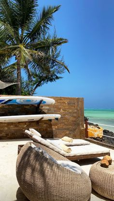 two lounge chairs sitting on top of a sandy beach next to the ocean with surfboards in the background