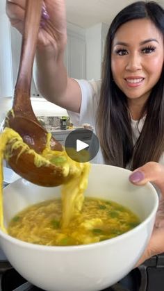 a woman is pouring yellow liquid into a white bowl with food in it while holding a wooden spoon