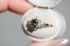 a close up of a person's hand holding a ring with a blue diamond in it