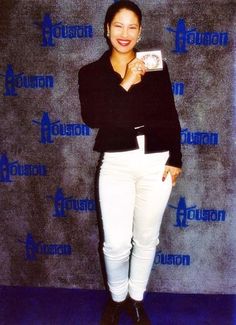 a woman standing in front of a blue and white backdrop holding up a small item