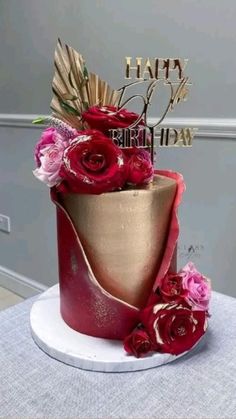 a red and gold birthday cake with flowers on it's top, sitting on a table