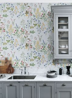 a kitchen with floral wallpaper and grey cupboards next to a white counter top