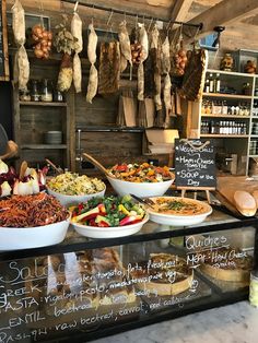 a display case filled with lots of different types of food in bowls next to meat hanging from the ceiling