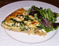 a white plate topped with a slice of quiche next to a leafy salad