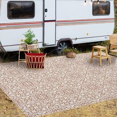 an rv is parked in the grass with two chairs and a table next to it