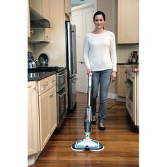 a woman standing in a kitchen with a mop on the floor next to her