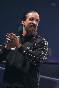 a man with a goatee standing in front of a wrestling ring holding his hands together