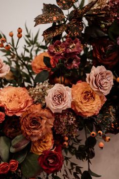 an arrangement of flowers and greenery on a table with white wall in the background