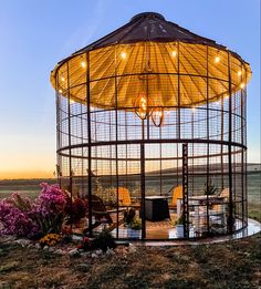 a gazebo sitting on top of a grass covered field next to flowers and trees