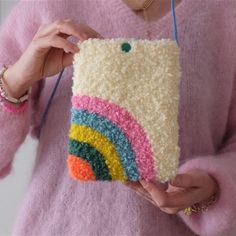 a woman is holding a crocheted phone case with a rainbow design on it