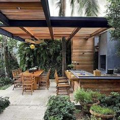 an outdoor kitchen and dining area with wooden tables and chairs, surrounded by greenery