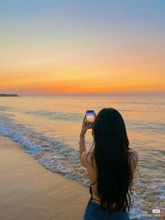 a woman standing on top of a beach holding a cell phone