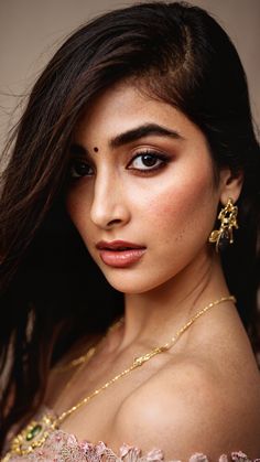 a woman with long dark hair wearing gold jewelry and a pink dress is looking at the camera