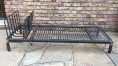 a metal bed frame sitting on top of a stone floor next to a brick wall