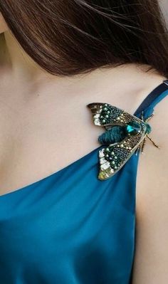 a woman wearing a blue dress with a butterfly brooch on it's back