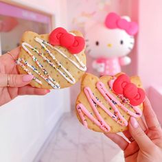 two hello kitty cookies with icing and sprinkles are being held up