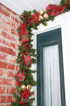 a christmas garland hanging from the side of a brick building with pine cones and bells on it