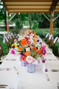 a long table is set with flowers and place settings for the guests to sit at