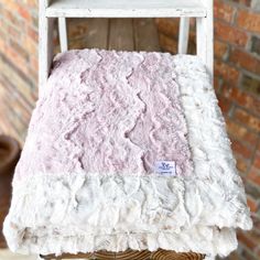 a white chair with a pink blanket sitting on it's back in front of a brick wall