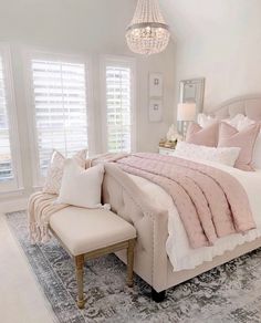 a bedroom with a large bed, chandelier and two windows that have white shutters