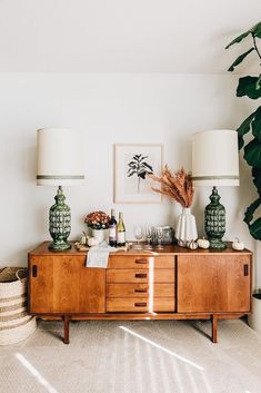 a living room with two lamps on top of a wooden cabinet next to a plant