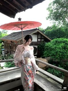 a woman in a kimono holding an umbrella over her head while standing on a porch