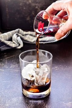 someone is pouring something into a glass with ice cubes