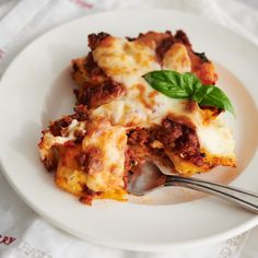 a white plate topped with lasagna covered in sauce and cheese next to a fork