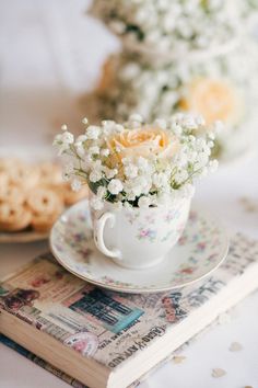 a cup with flowers in it sitting on top of a plate next to a book