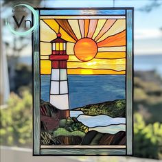 a stained glass window with the sun setting over water and a lighthouse in the background