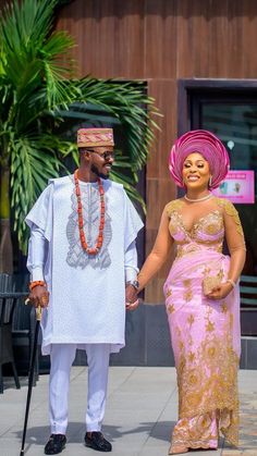 a man and woman dressed in traditional african garb holding hands while standing next to each other