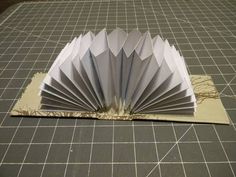 an origami fan sitting on top of a piece of paper next to a cutting board