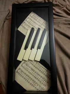 four pieces of sheet music are arranged in a black frame on a bed with sheet music notes