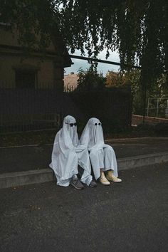 two people dressed in white sitting on the side of a road next to a tree