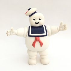 a white plastic toy with an apron and hat on it's head, arms outstretched