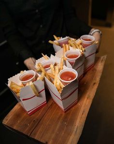 french fries with ketchup and mustard are on a wooden tray in front of a man