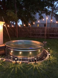 an outdoor hot tub lit up at night with string lights on the fence and trees in the background