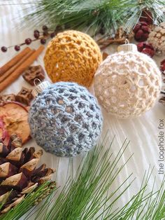 three crocheted ornaments sitting next to pine cones and cinnamons on a table