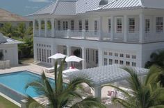 an aerial view of a large white house with a pool in the foreground and palm trees surrounding it